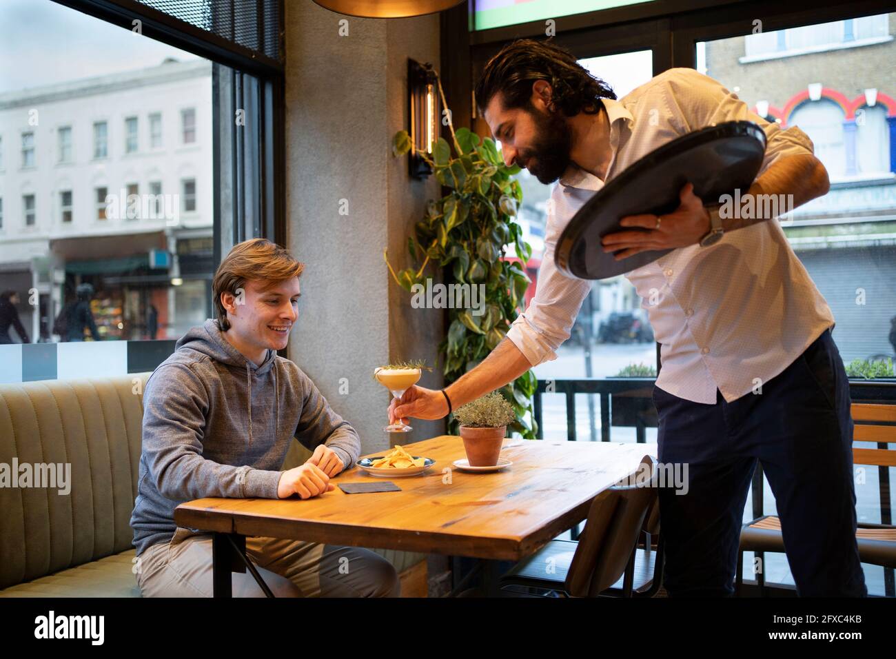 Ein männlicher Kellner serviert jungen Gästen Getränke in der Bar Stockfoto