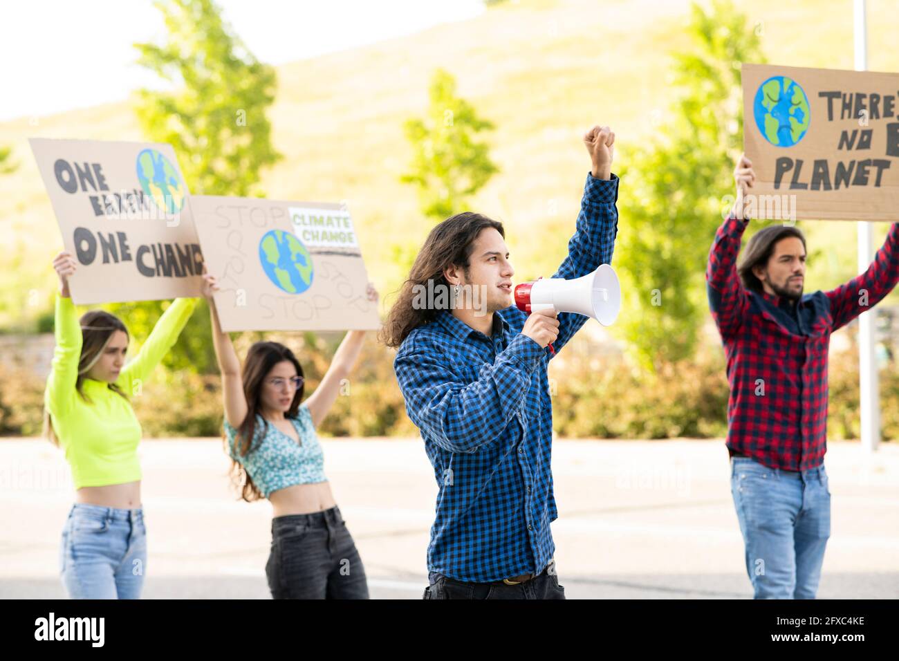 Junger männlicher Aktivist, der gegen den Klimawandel protestiert, wobei männliche und weibliche Demonstranten auf dem Weg sind Stockfoto