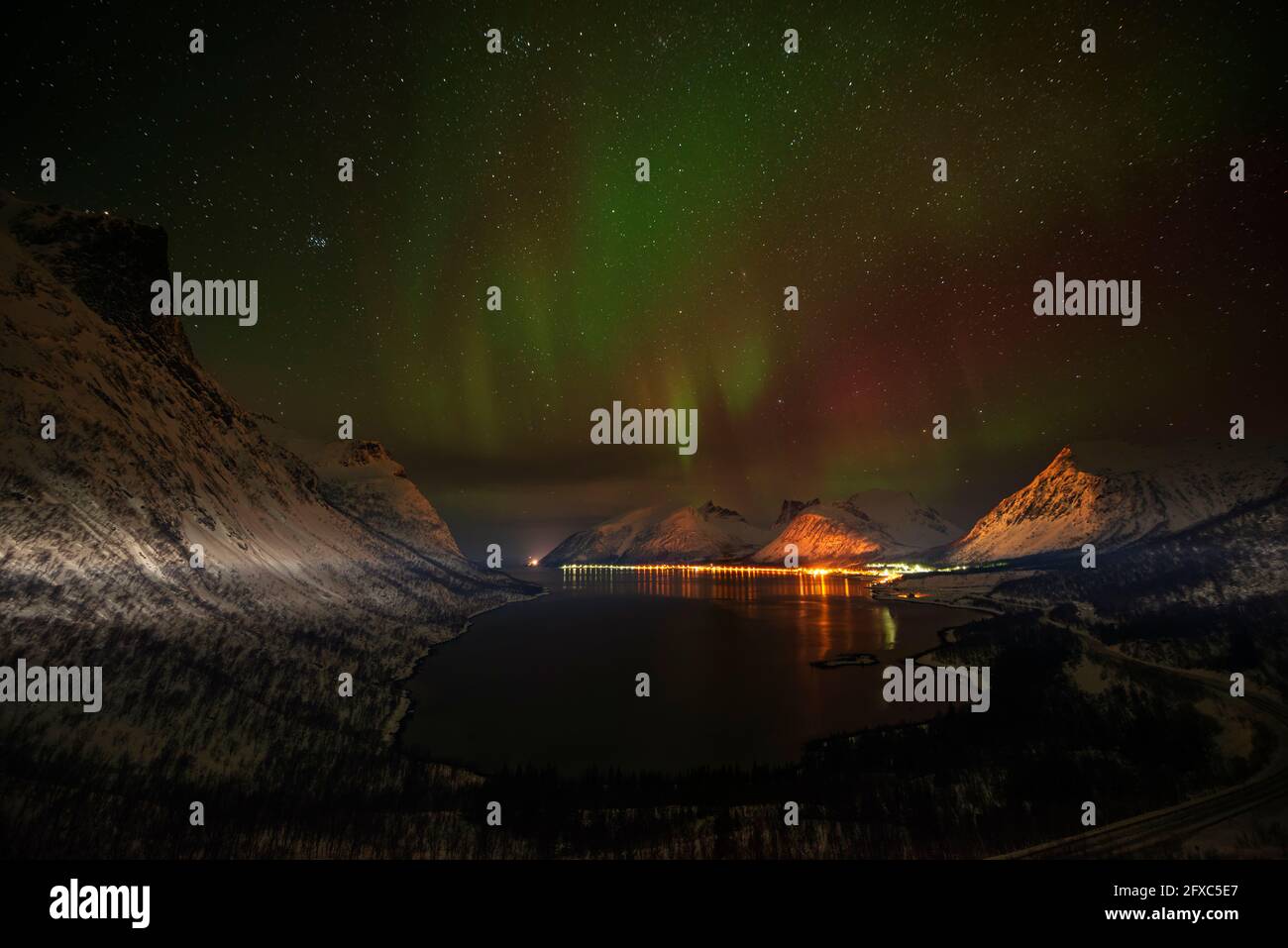 Norwegen, Tromso, Bergsbotn, Panoramaaussicht auf Aurora Borealis über dem beleuchteten Fjorddorf auf Senja Island Stockfoto