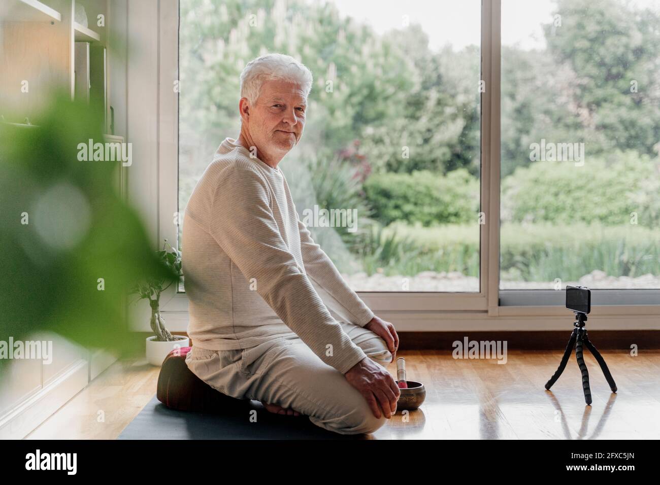 Leitender männlicher Influencer vloggt über das Mobiltelefon, während er auf der Trainingsmatte sitzt Stockfoto