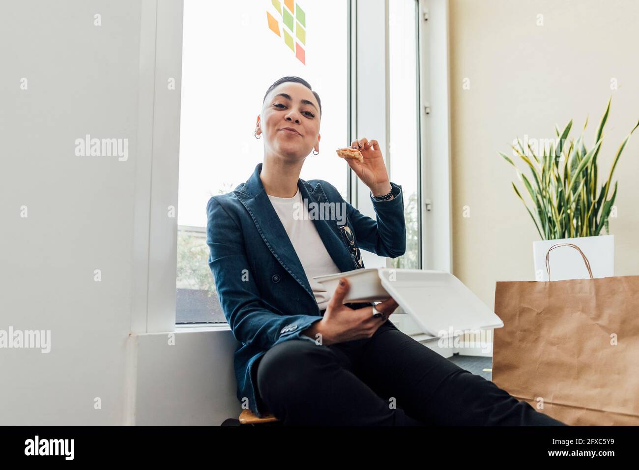 Junger Unternehmer, der im Büro sitzt und Essen hat Stockfoto