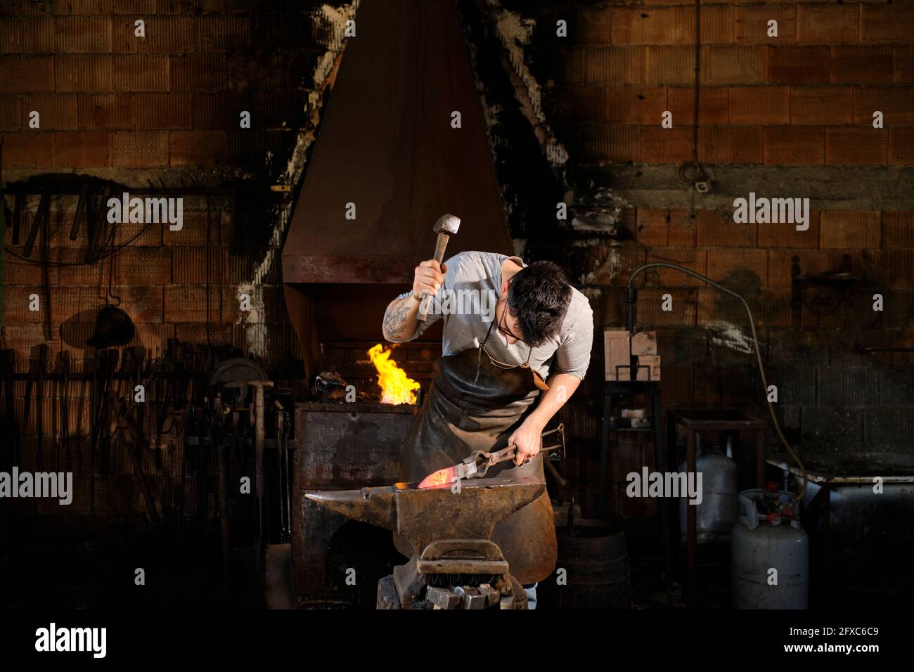 Männlicher Metallarbeiter, der in der Schmiede Metall mit Hammer schmiedet Stockfoto