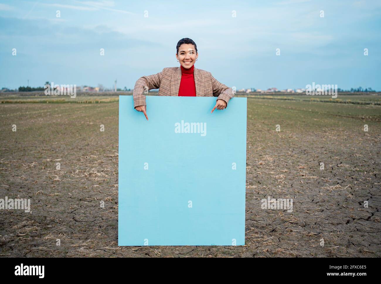 Lächelnde Frau, die auf das blaue Gemälde auf dem Feld zeigt Stockfoto