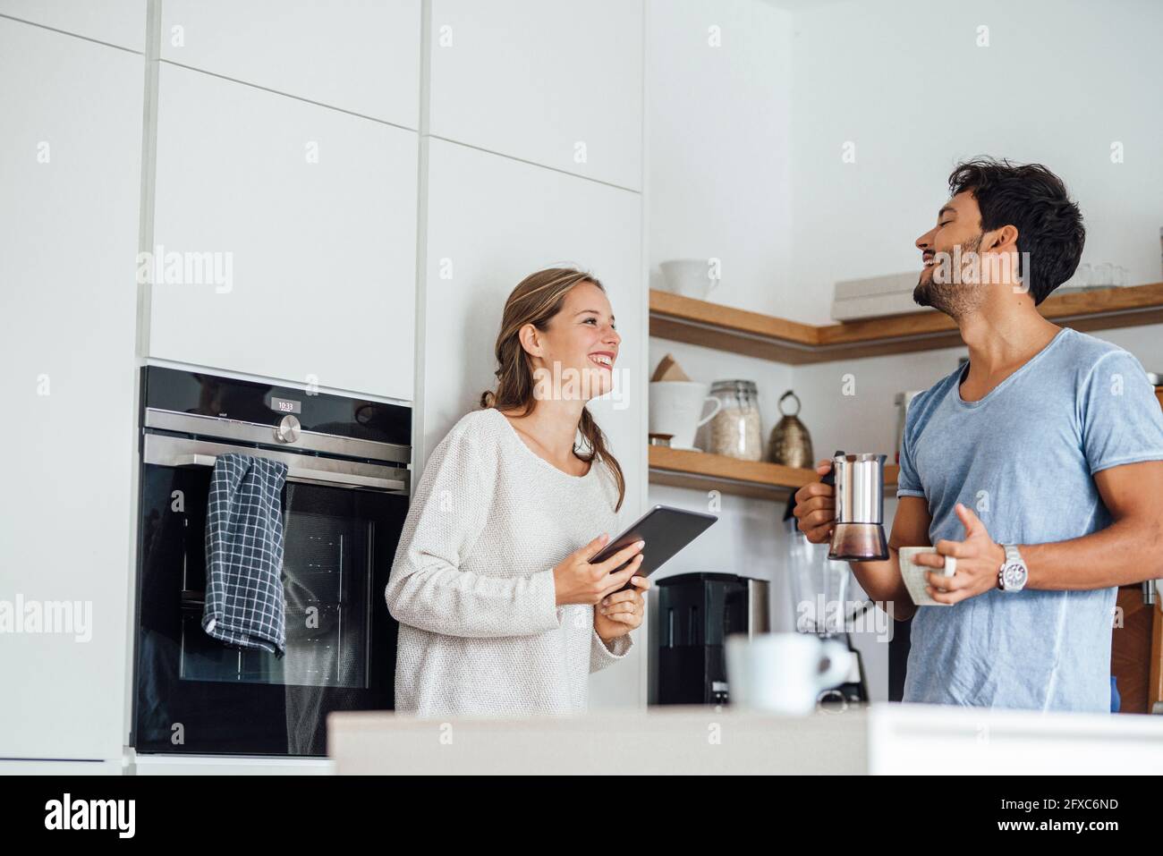 Fröhliches junges Paar, das sich ansieht, während es in der heimischen Küche steht Stockfoto