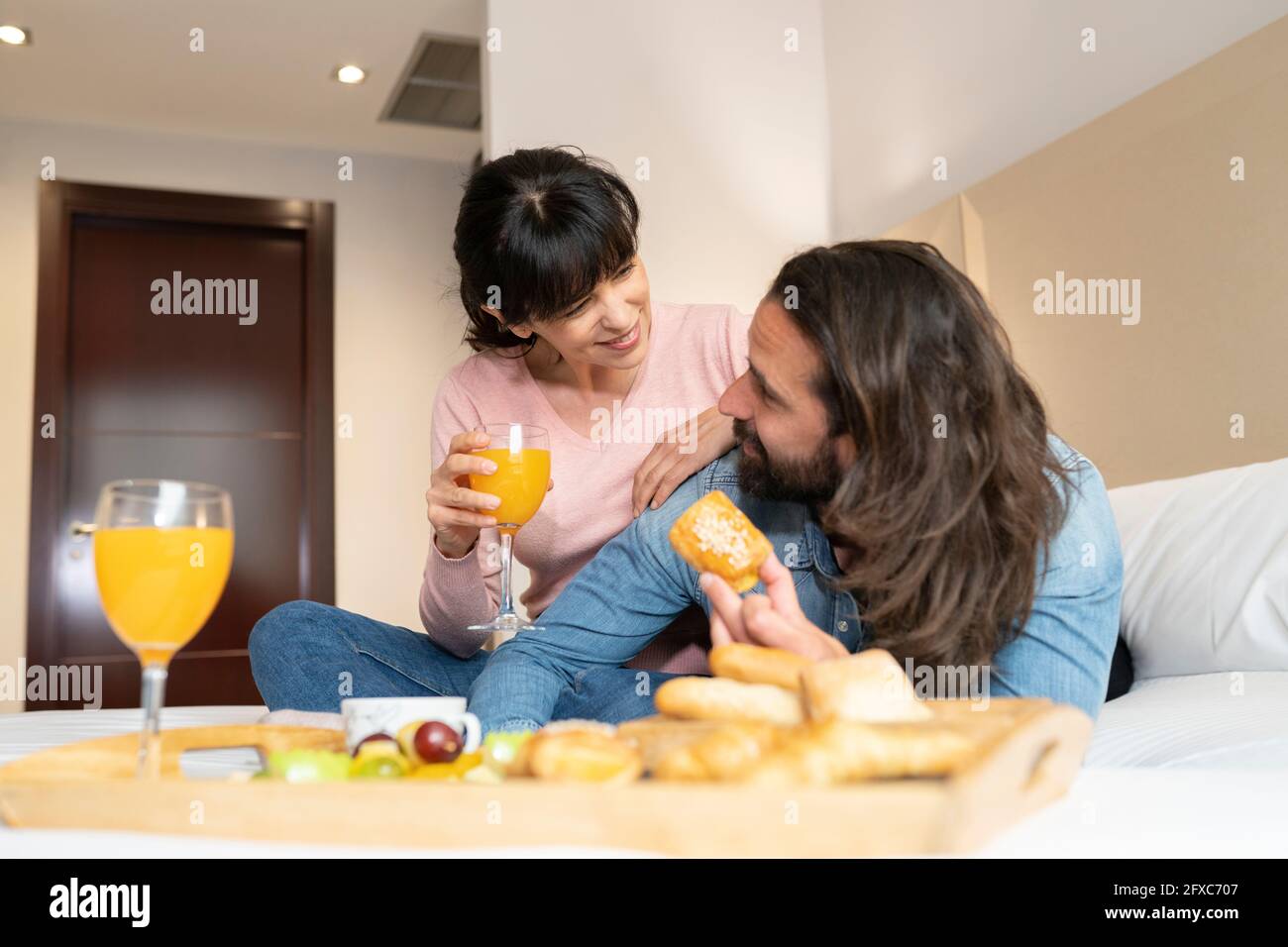 Lächelndes Paar, das sich beim Frühstück auf dem Bett in der Hotelsuite ansah Stockfoto