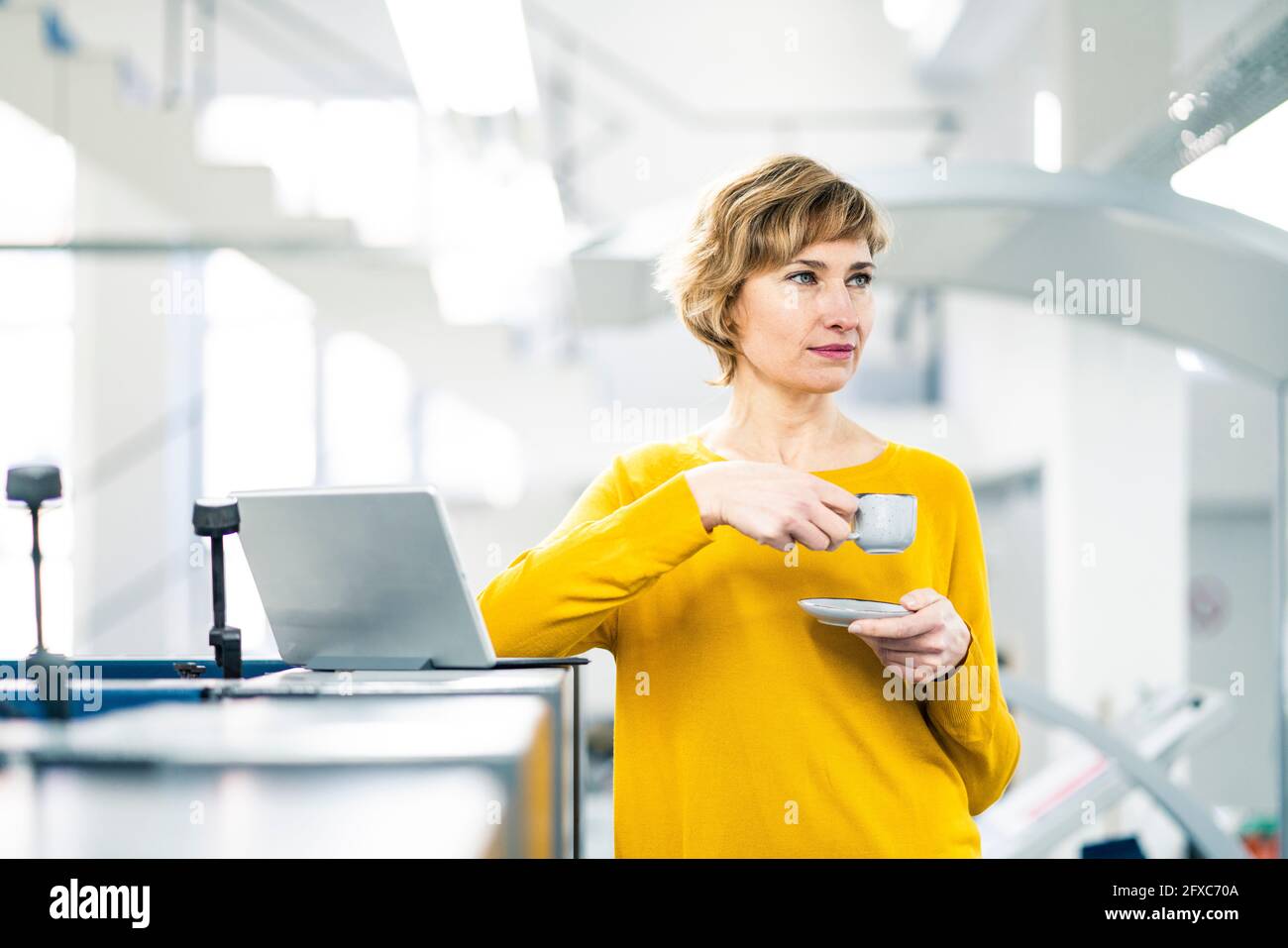 Nachdenkliche Geschäftsfrau mit Kaffeetasse, die in der Werkstatt steht Stockfoto