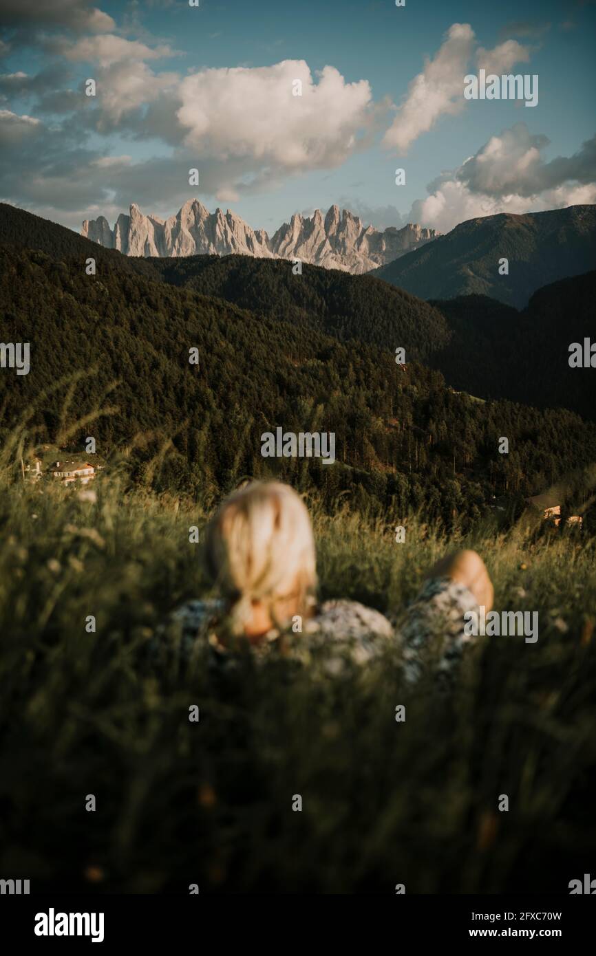 Frau, die auf Gras liegt, während sie die dolomitenberge in Südtirol, Italien, betrachtet Stockfoto
