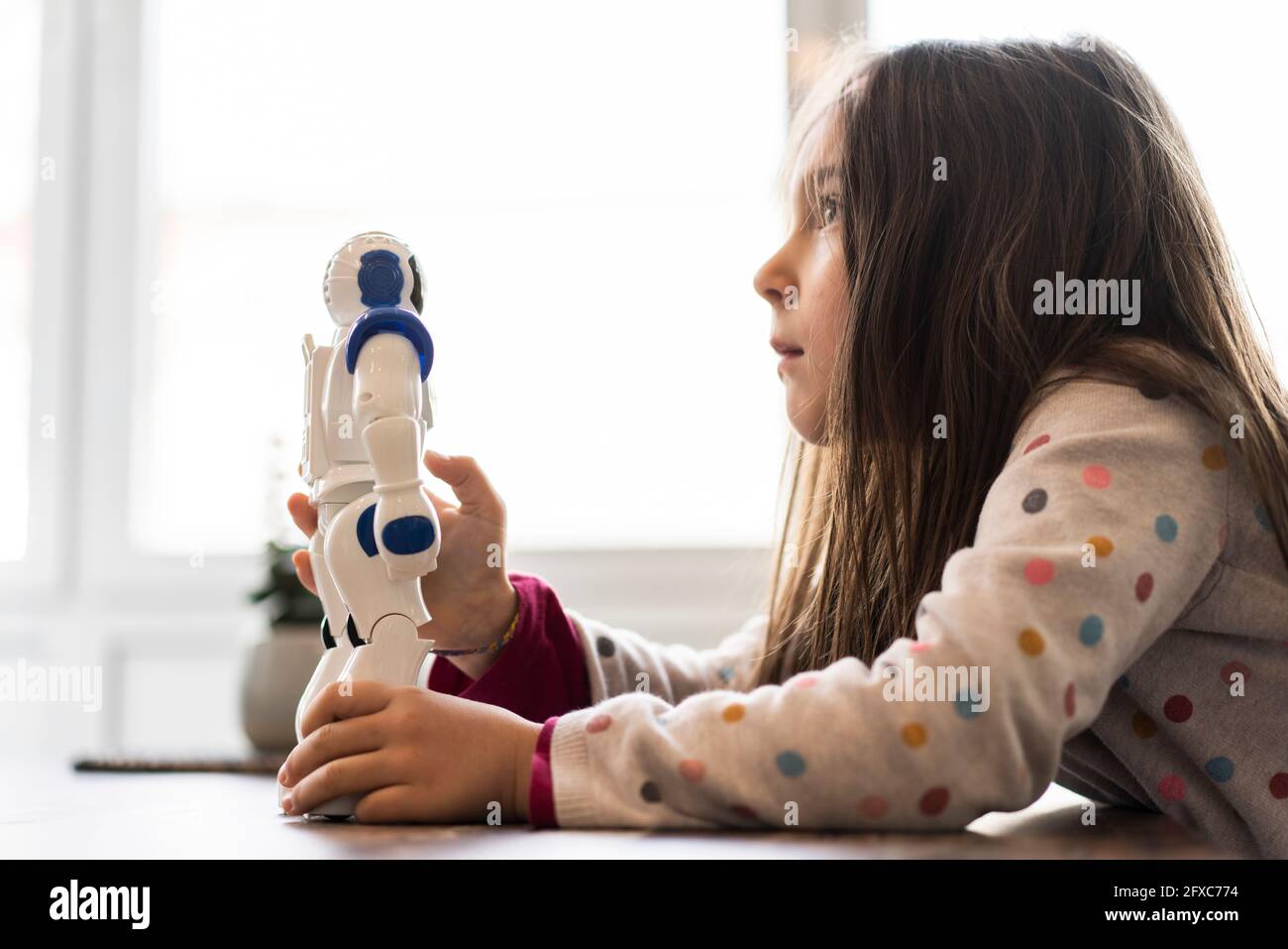 Nachdenkliches Mädchen, das wegschaut, während es Roboterspielzeug zu Hause hält Stockfoto
