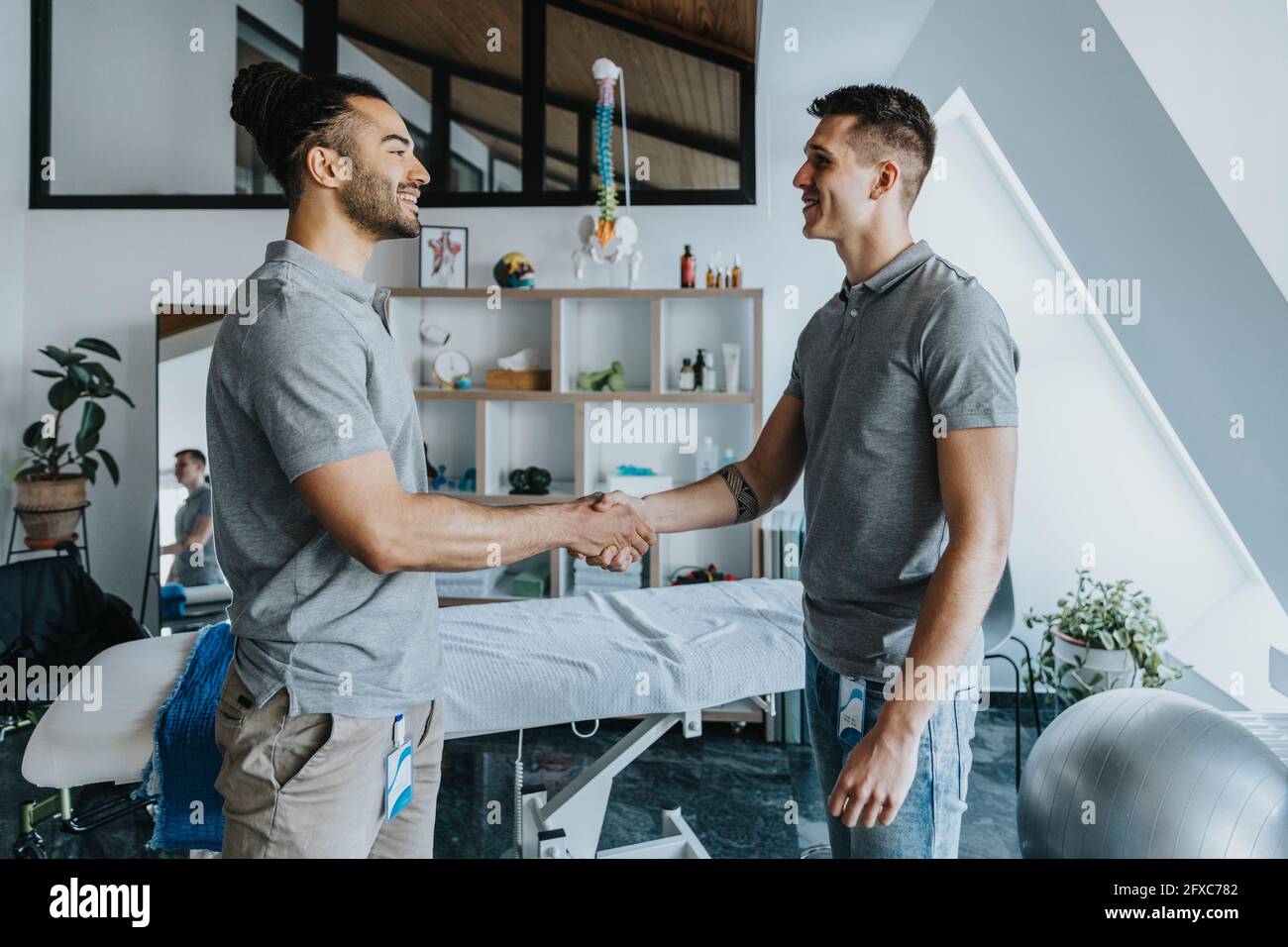 Männliche Physiotherapeuten lächeln, während sie in der Praxis die Hände schütteln Stockfoto