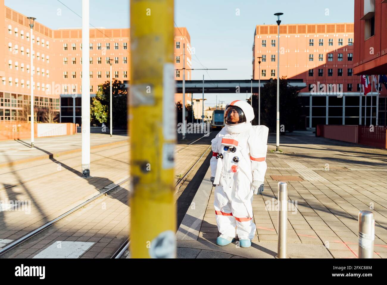 Die Astronautin schaut weg, während sie in der Nähe der Straßenbahnlinien auf dem Fußweg in der Stadt steht Stockfoto