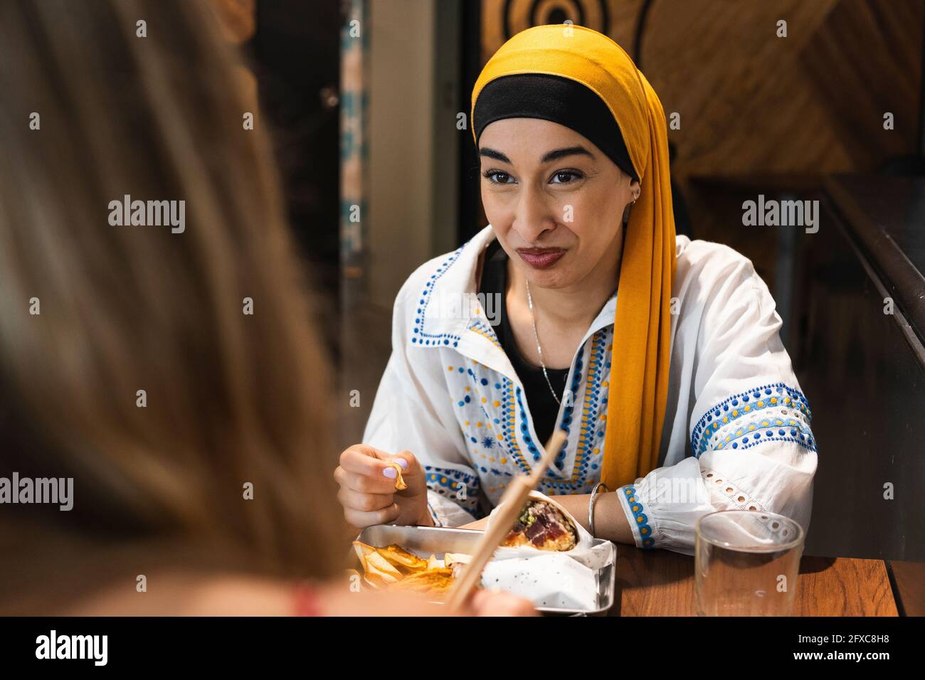 Junge Frau mit Kopftuch, die eine Freundin anschaut, während sie im Restaurant essen geht Stockfoto