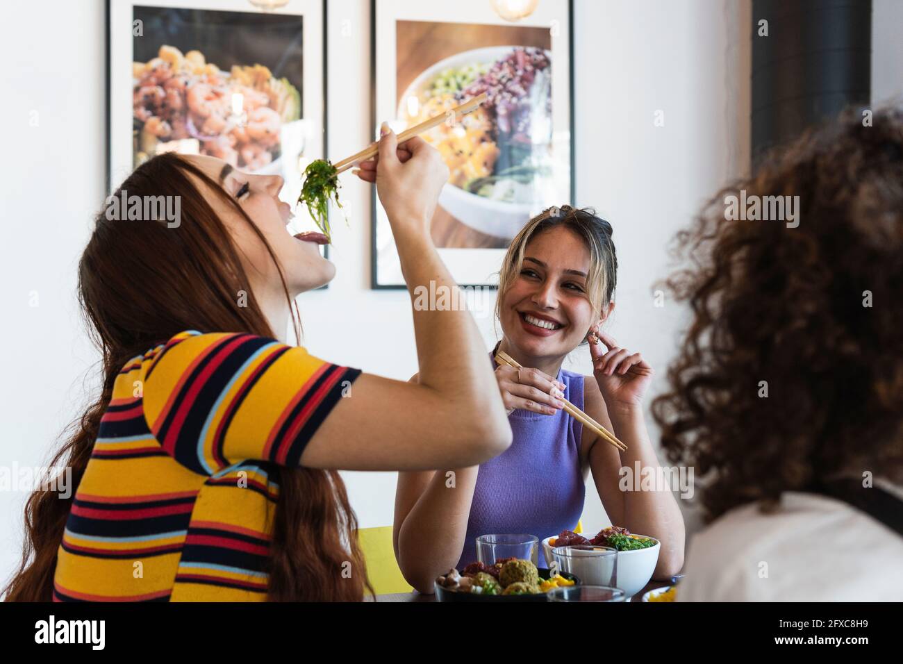 Lächelnde junge Frau, die eine Freundin beim Essen mit Essstäbchen im Restaurant ansieht Stockfoto