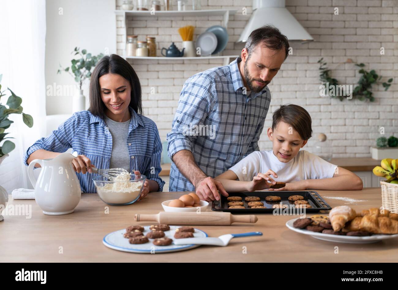 Vater und Sohn schauten auf Keks, während Mutter Mehl in der Küche zu Hause mischte Stockfoto