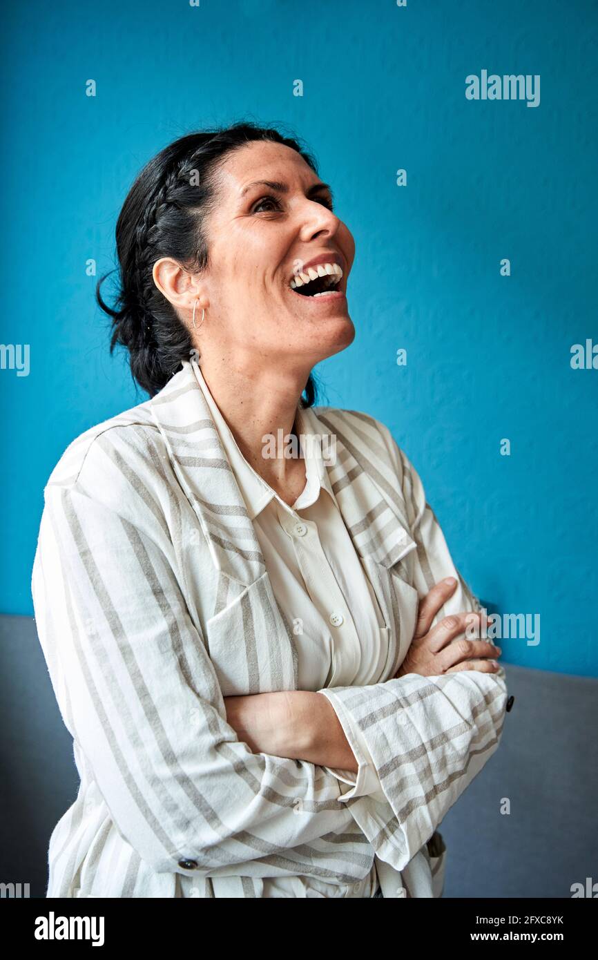 Frau mit gekreuzten Armen lachend vor der blauen Wand Stockfoto