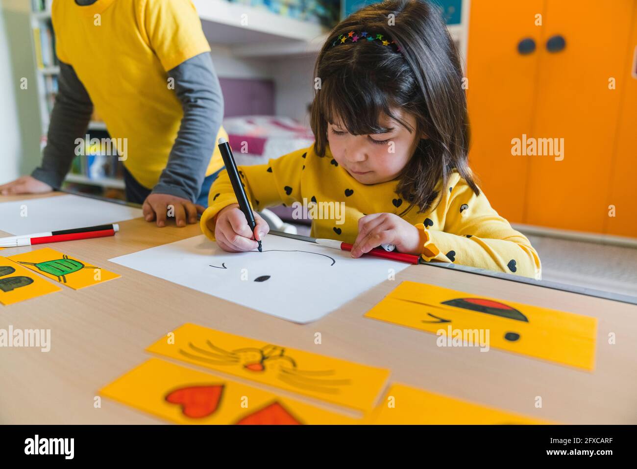 Mädchen zeichnen Smiley Gesicht auf Papier, während zu Hause spielen Stockfoto