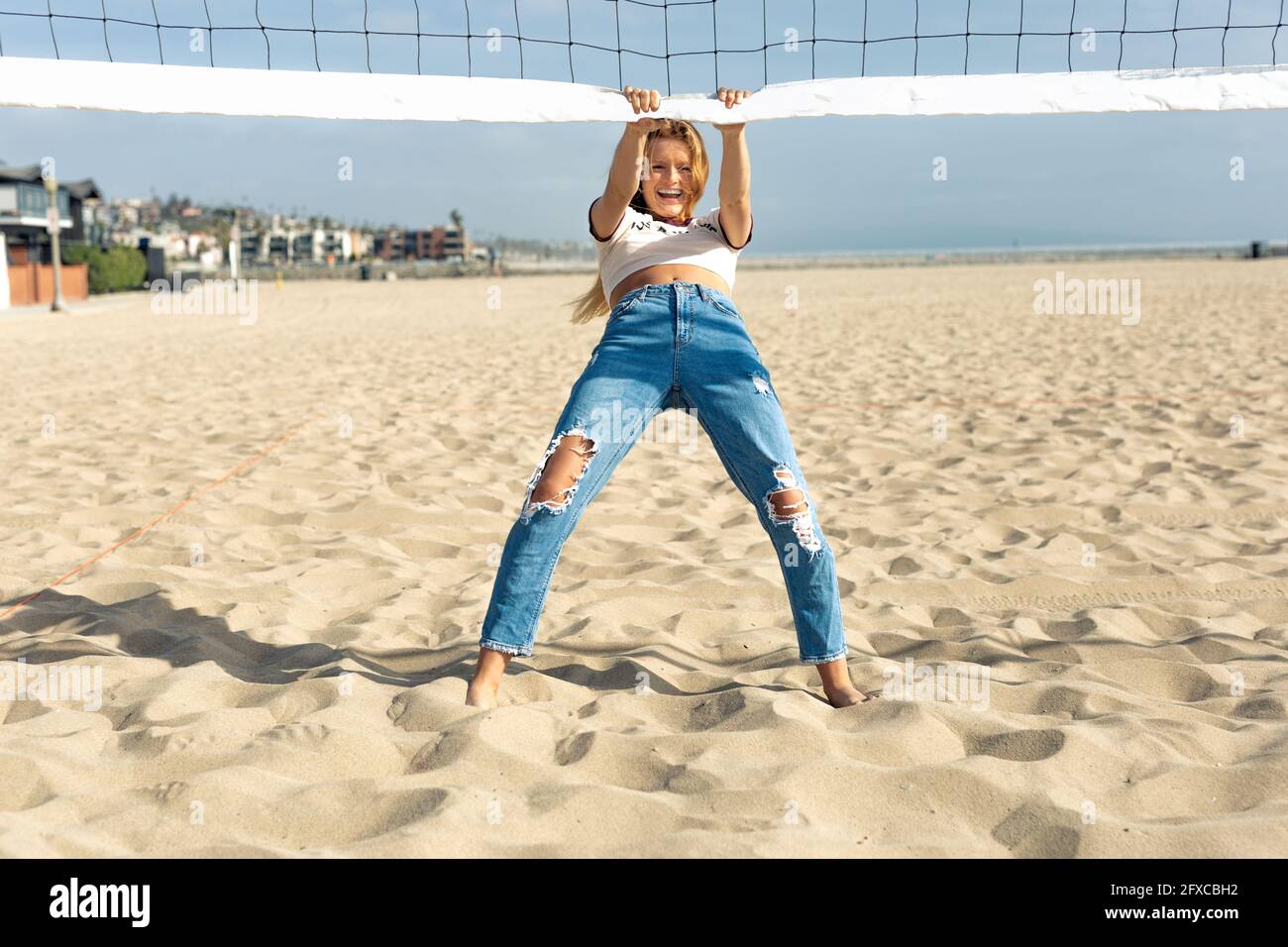 Fröhliche junge Frau, die sich an sonnigen Tagen am Strand am Volleyballnetz stützt Stockfoto