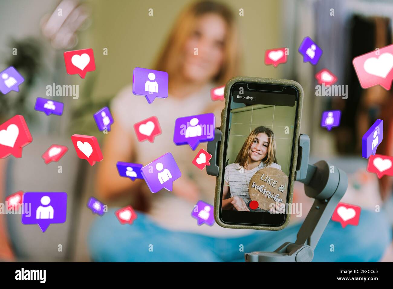Lächelndes Teenager-Mädchen auf dem Handy-Bildschirm inmitten von Social-Media-Symbolen zu Hause Stockfoto