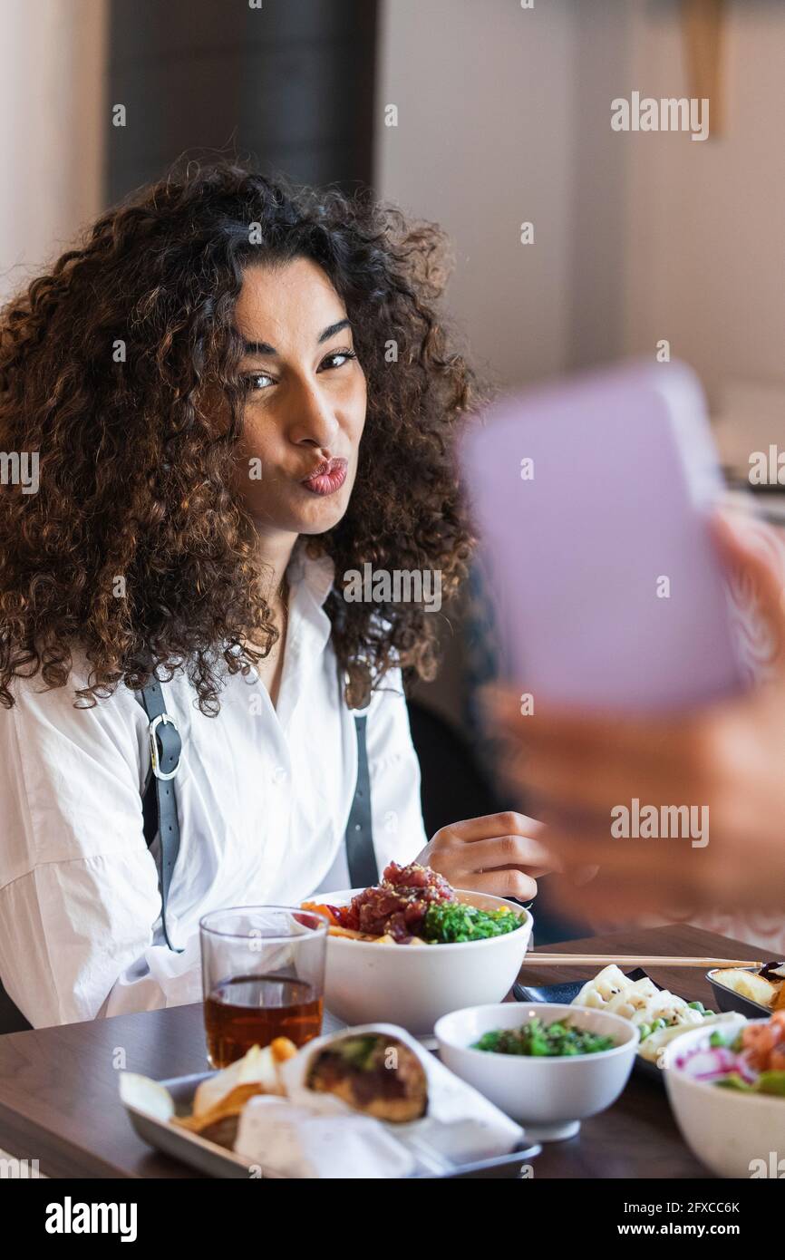 Eine Freundin fotografiert eine junge Frau, die mit Essen im Restaurant sitzt Stockfoto