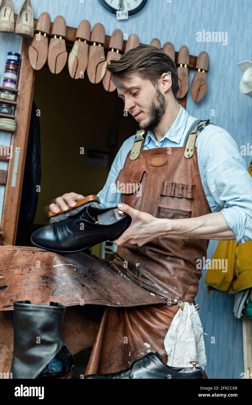 Männlicher Schuster in Schürze Polierschuh mit Pinsel in der Werkstatt Stockfoto