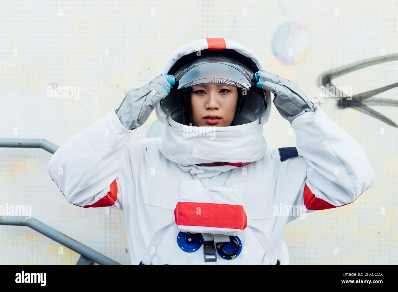 Weibliche Astronautin, die den Helm hält, während sie an der Wand steht Stockfoto