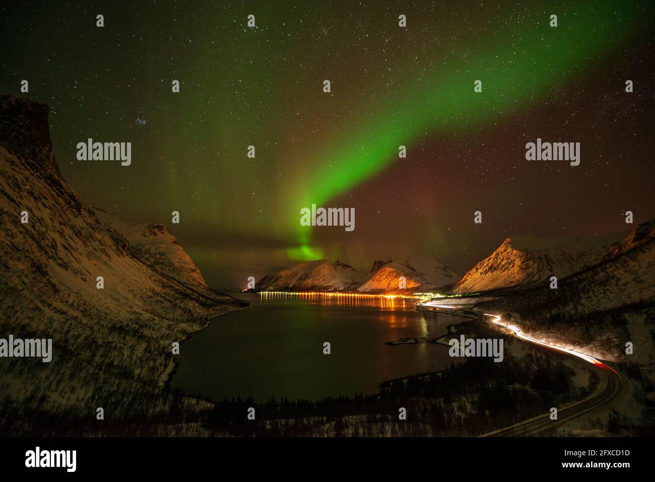 Norwegen, Tromso, Bergsbotn, Panoramaaussicht auf Aurora Borealis über dem beleuchteten Fjorddorf auf Senja Island Stockfoto