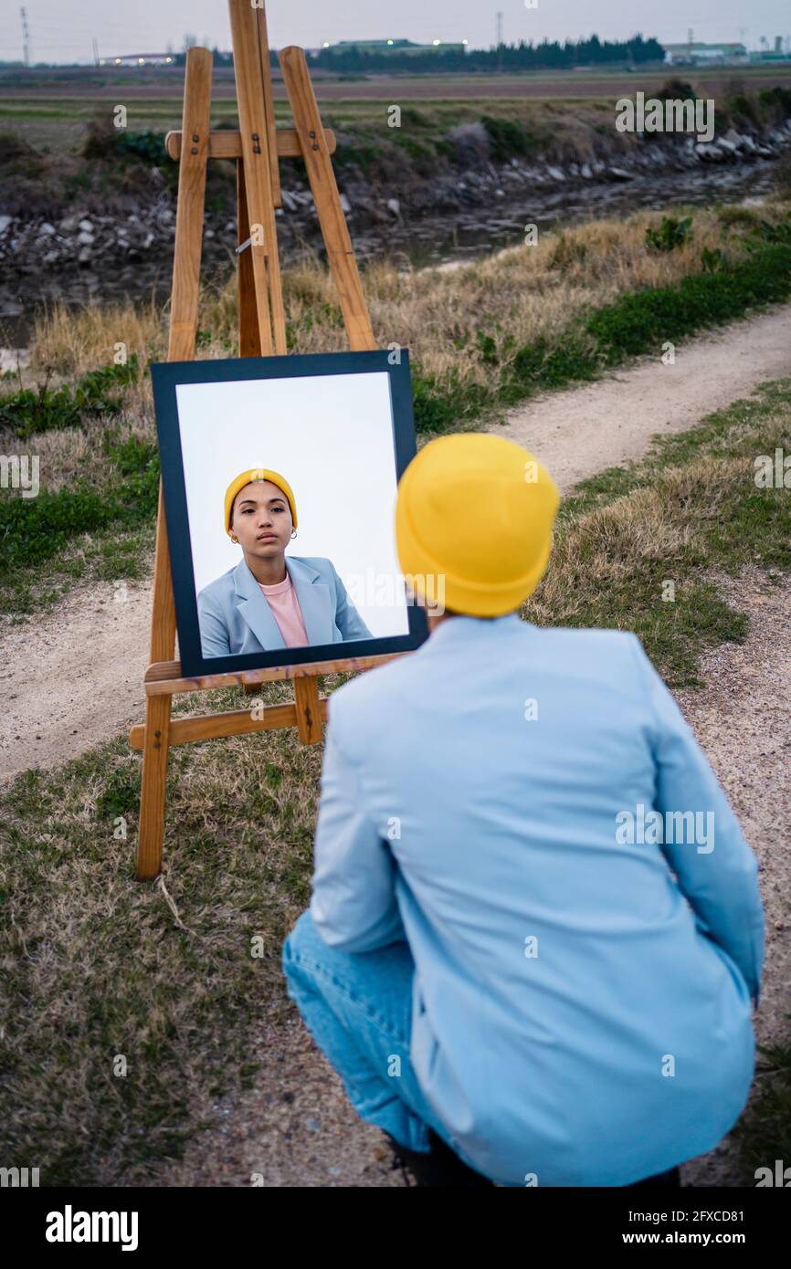 Frau, die die Reflexion im Spiegel auf dem Feld betrachtet Stockfoto