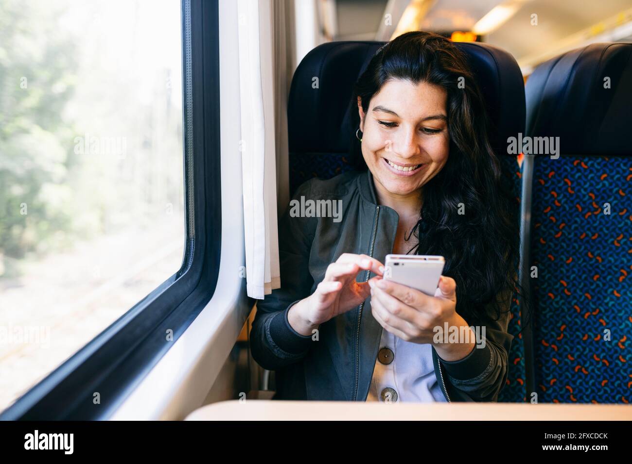 Glückliche Frau, die Smartphone benutzt, während sie im Zug sitzt Stockfoto