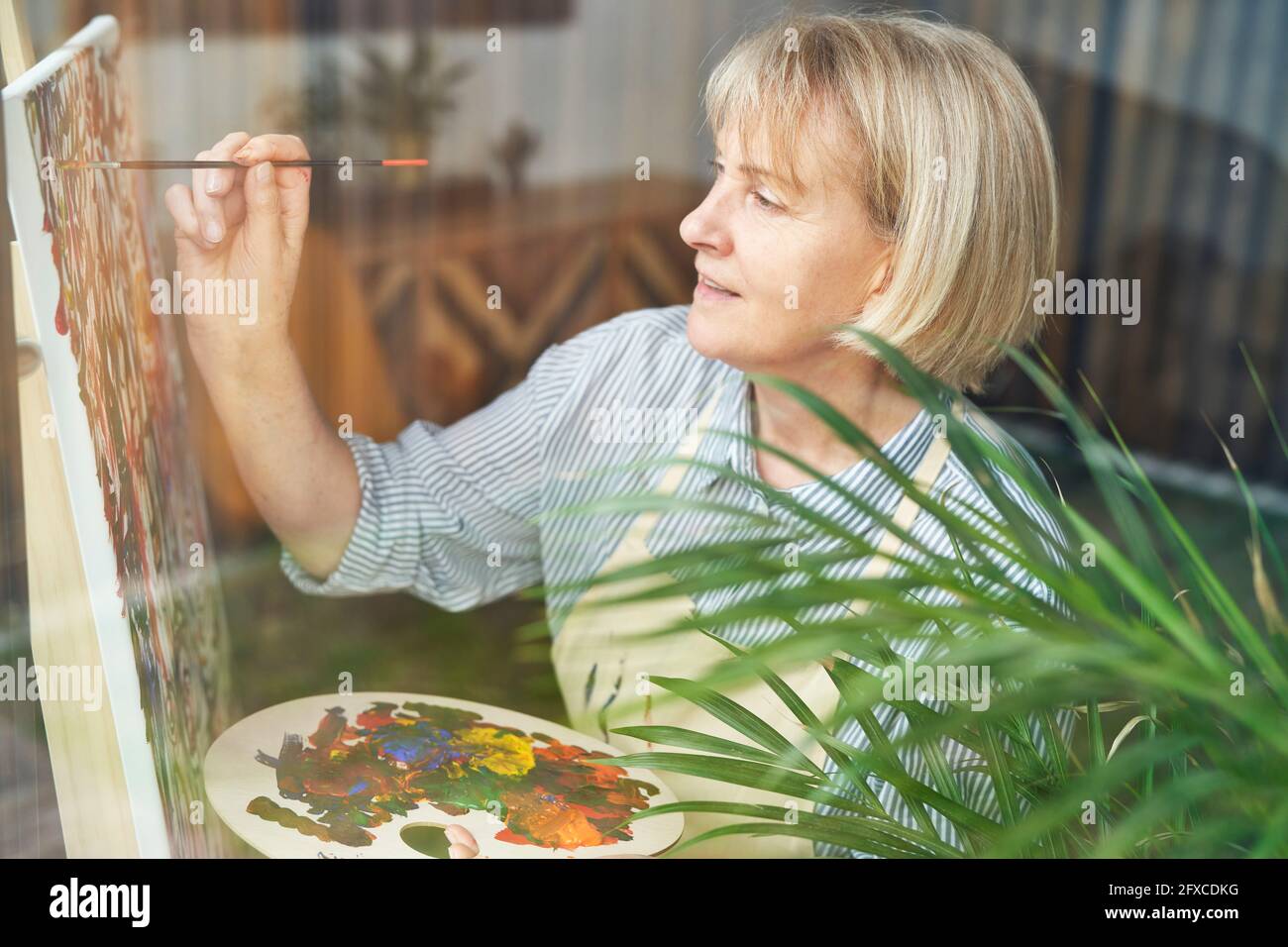 Reife Frau mit blonden Haaren auf Staffelei zu Hause malen Stockfoto