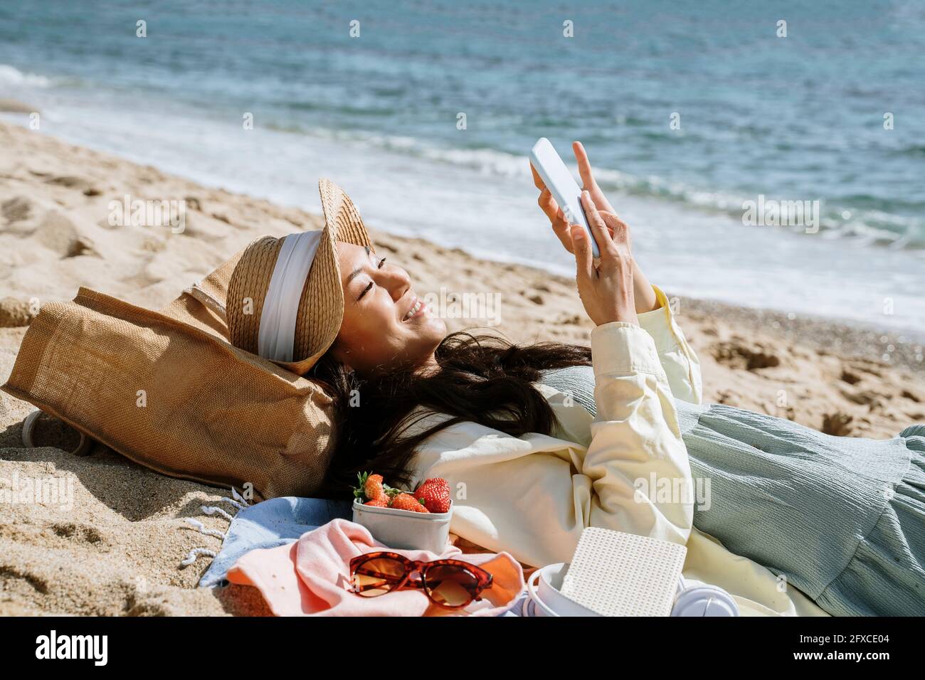 Frau, die Smartphone benutzt, während sie am Strand auf Sand liegt Stockfoto