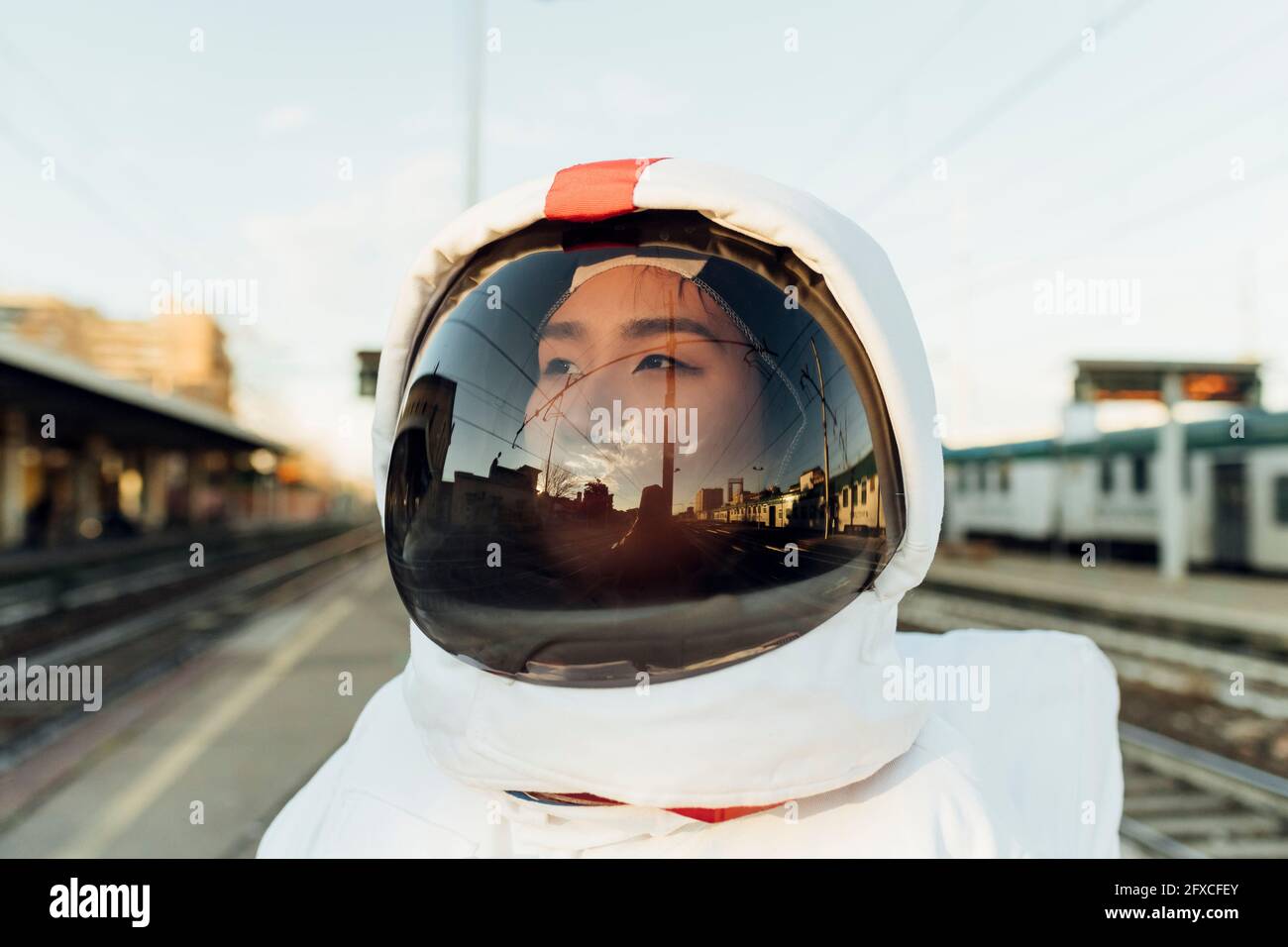 Nachdenkliche Astronautin im Weltraumhelm, die während des Sonnenuntergangs wegschaut Stockfoto
