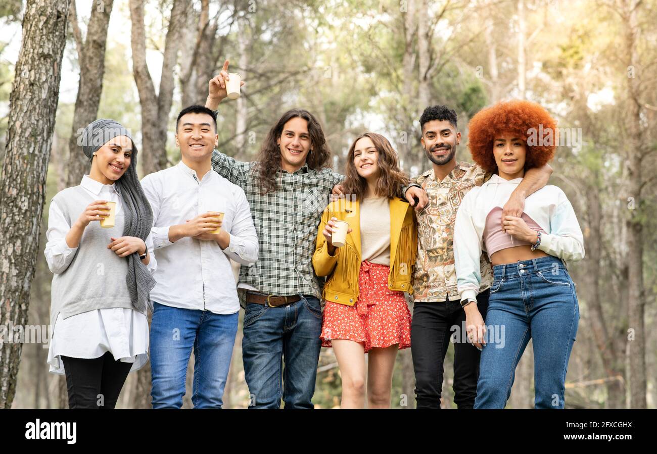 Fröhliche männliche und weibliche Freunde halten wiederverwendbares Glas im Wald Stockfoto