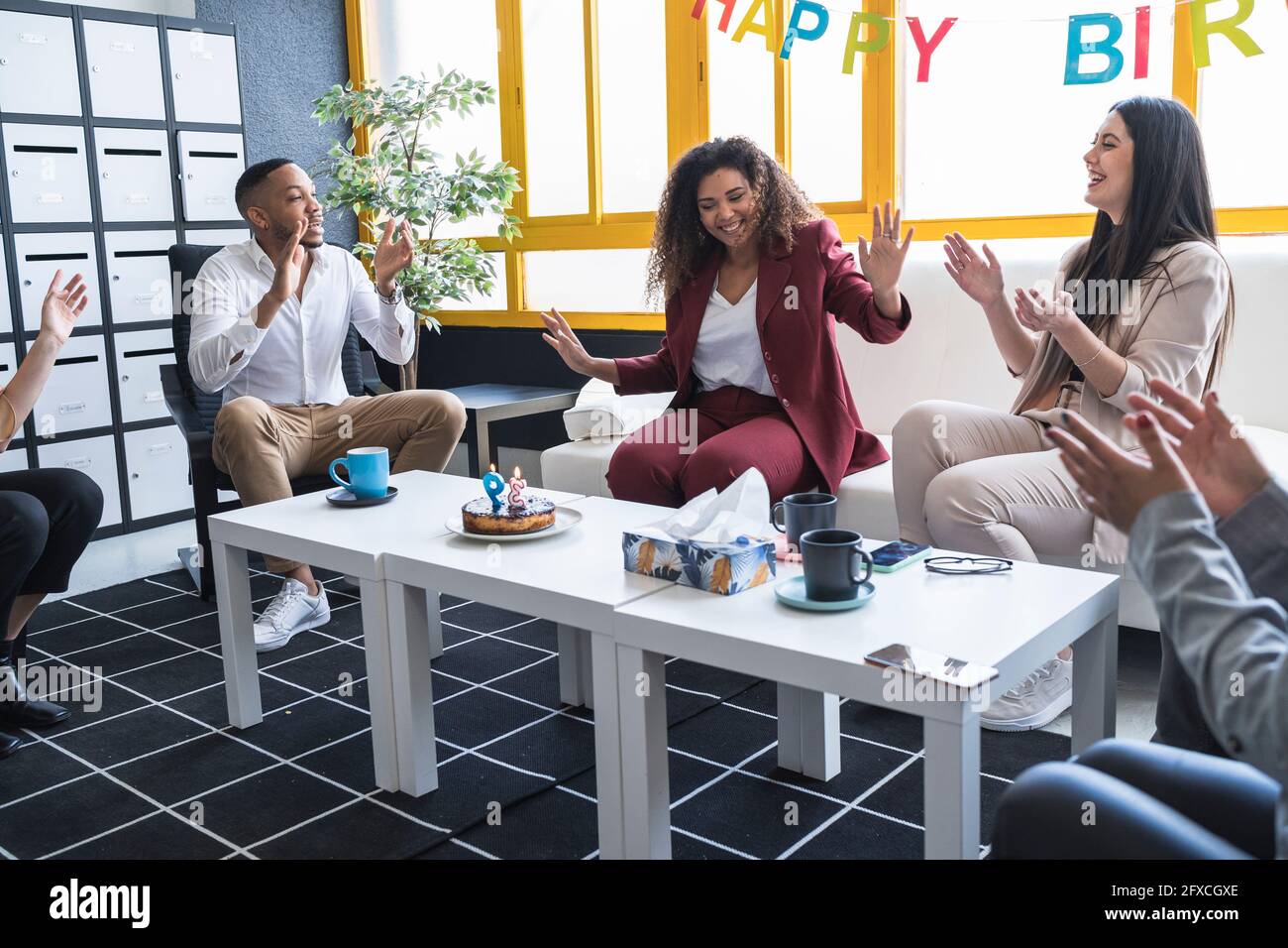 Lächelnde Geschäftsfrau, die Kollegen beim Klatschen während der Geburtstagsfeier im Büro mit einer Stoppgeste zeigt Stockfoto