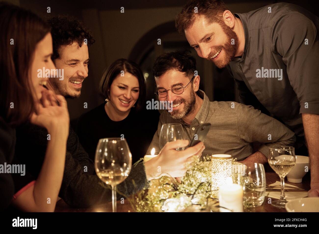 Mann mittleren Erwachsenen, der männlichen und weiblichen Freunden am Esstisch das Mobiltelefon zeigt Stockfoto