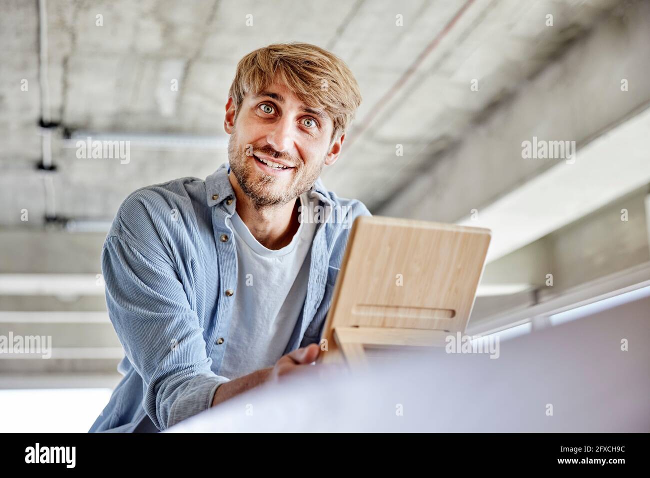 Lächelnder Mann mit grauen Augen, der Holzmaterial auf dem Dachboden hält Stockfoto