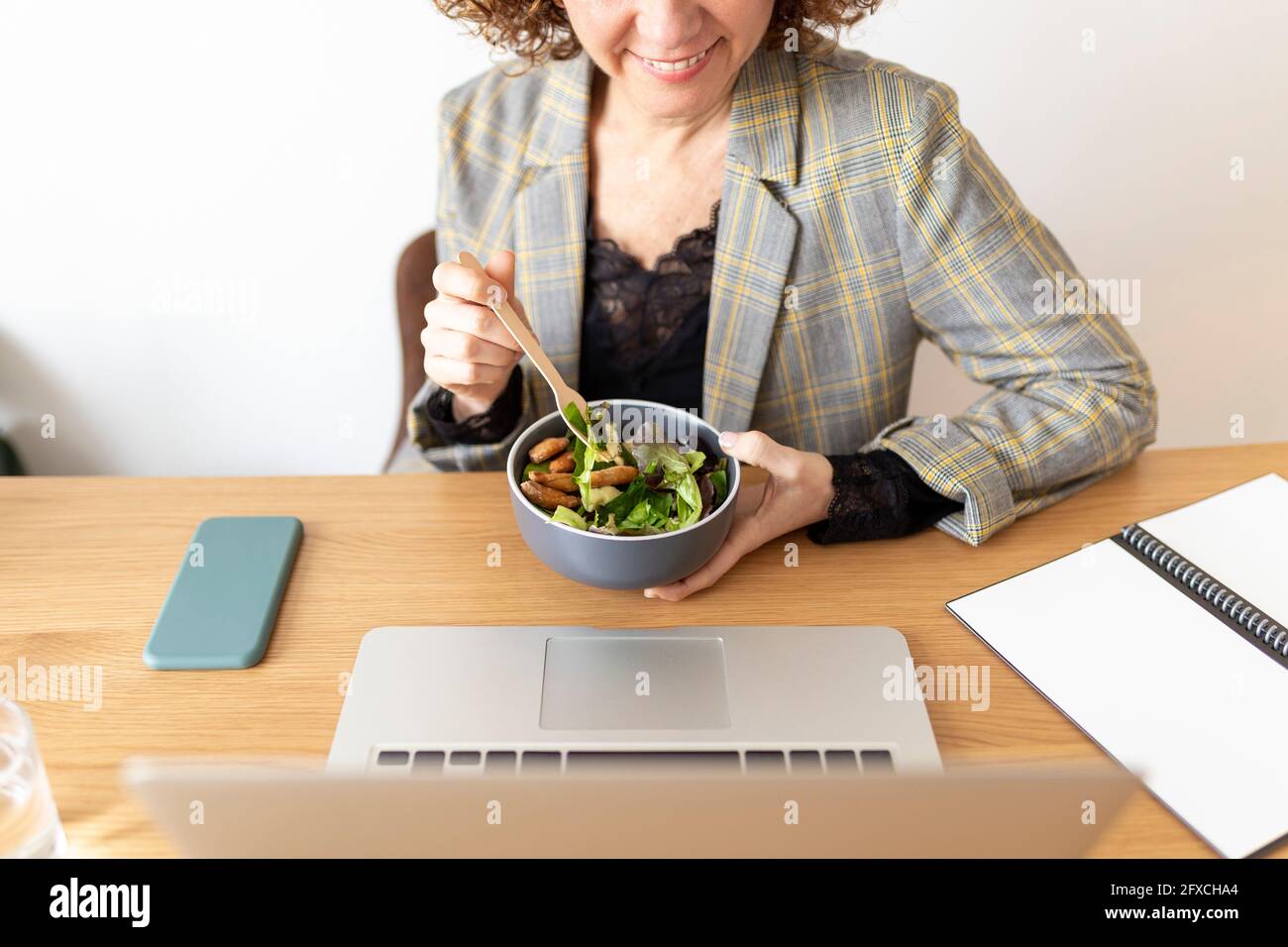 Weibliche Freiberuflerin hält Schüssel mit Essen auf dem Tisch zu Hause Stockfoto