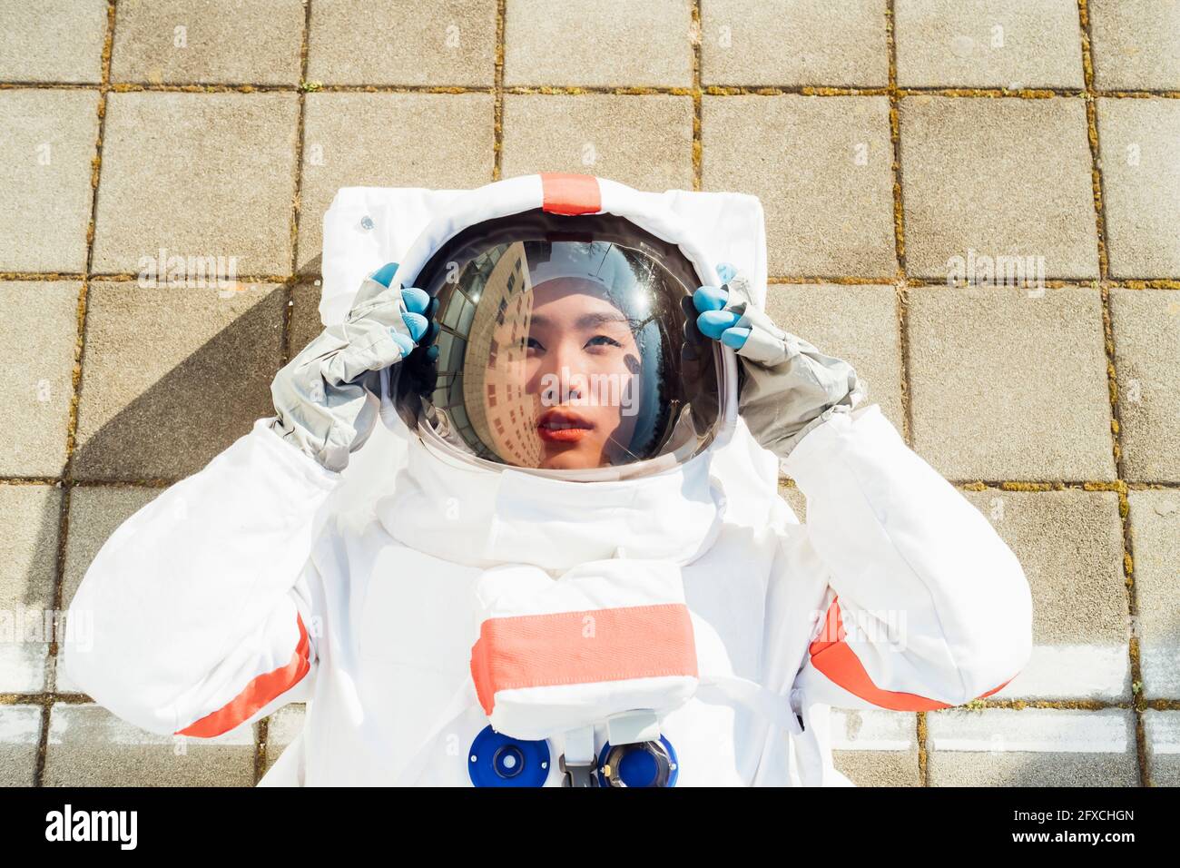 Weibliche Astronautin mit Helm, während sie an sonnigen Tagen auf dem Fußweg liegt Stockfoto