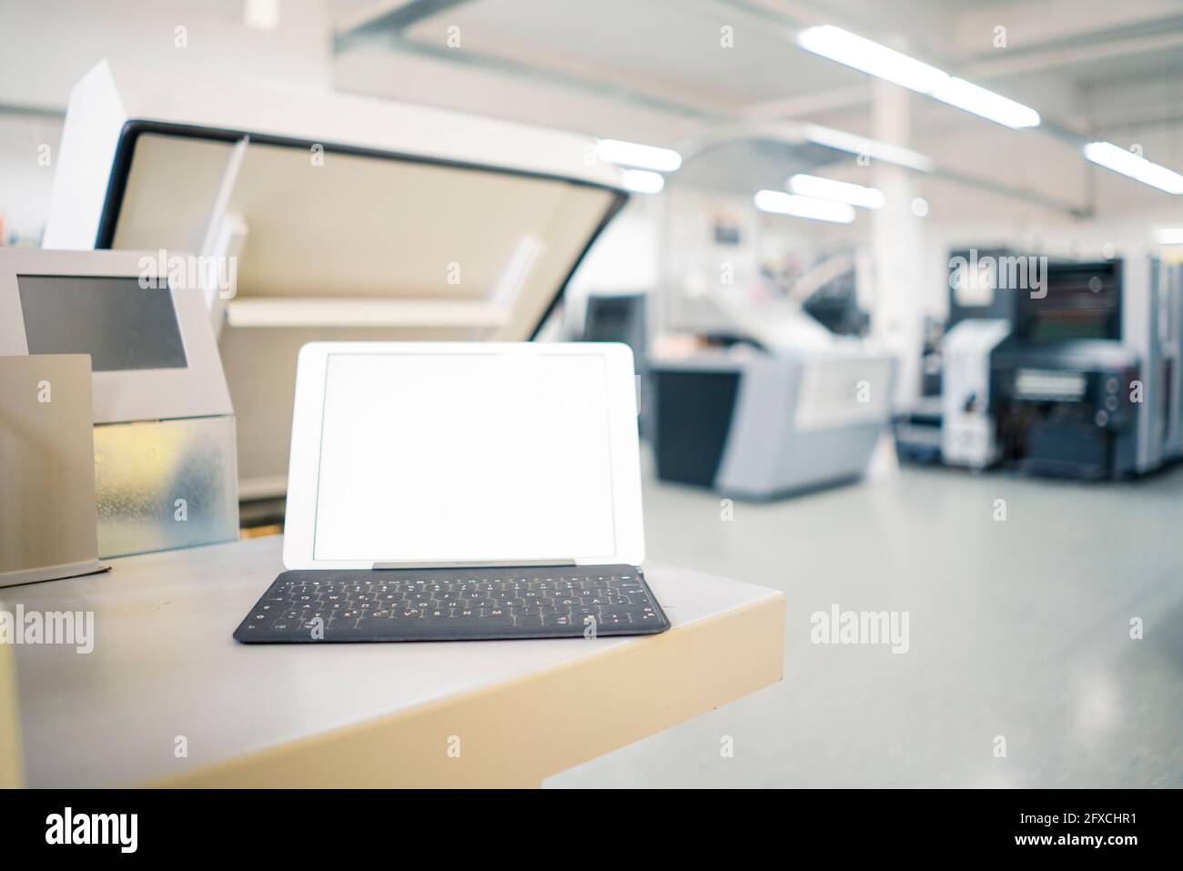 Digitales Tablet auf dem Tisch mit Druckmaschine im Werk Stockfoto