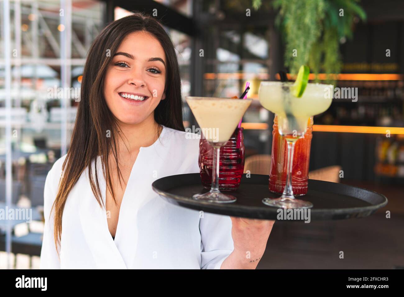 Lächelnder, schöner Barkeeper, der an der Bar ein Tablett mit Cocktails hält Stockfoto