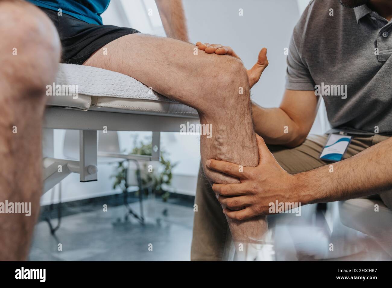 Physiotherapeut berührt Knie des männlichen Patienten in der Praxis Stockfoto