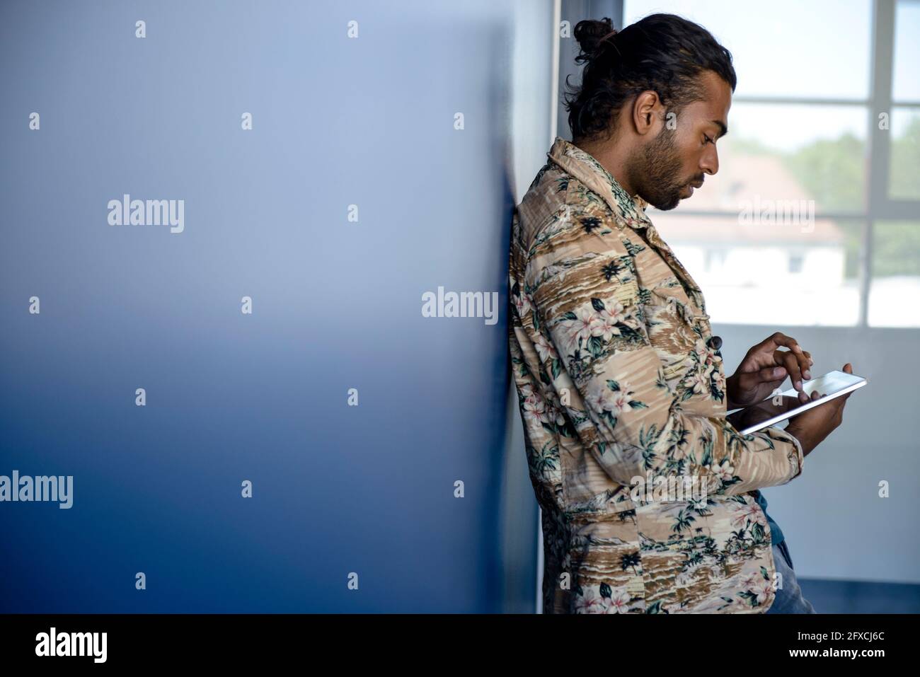 Mann in legerer Kleidung mit digitalem Tablet, während er sich an die Wand lehnt Stockfoto