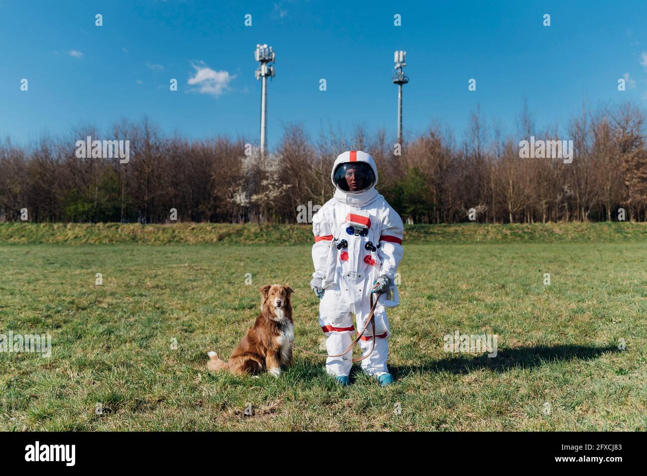 Astronautin im Raumanzug, der mit Hund auf Gras steht Stockfoto