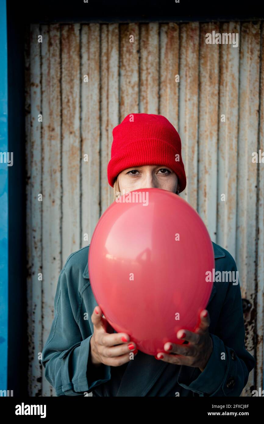 Frau mit mittlerem Erwachsenen, die einen roten Ballon vor Wellblech hält Stockfoto