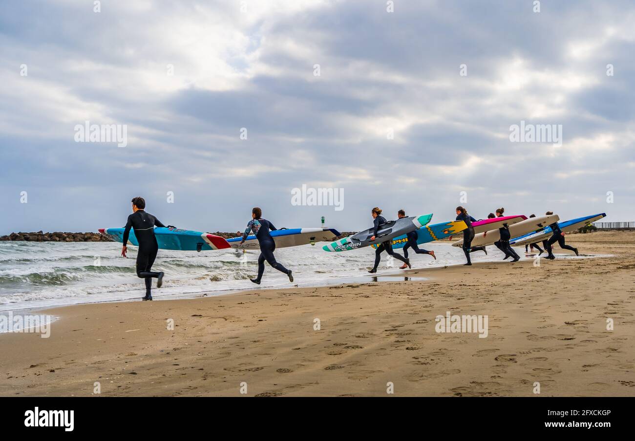 Surfer an einem Strand, der mit Surfbrettern zum Meer läuft An einem bewölkten Tag Stockfoto
