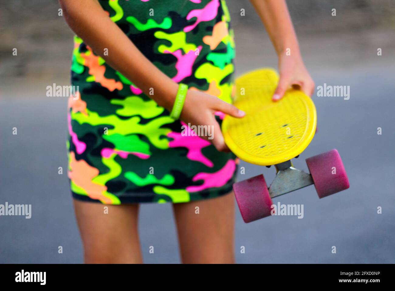 Defokussieren Mädchen mit gelben Penny Board. Vorderansicht. Jugend-Hipster-Kultur. Kinderhände halten tagsüber ein kurzes Cruiser-Pennyboard im Freien. Sporthobby Stockfoto