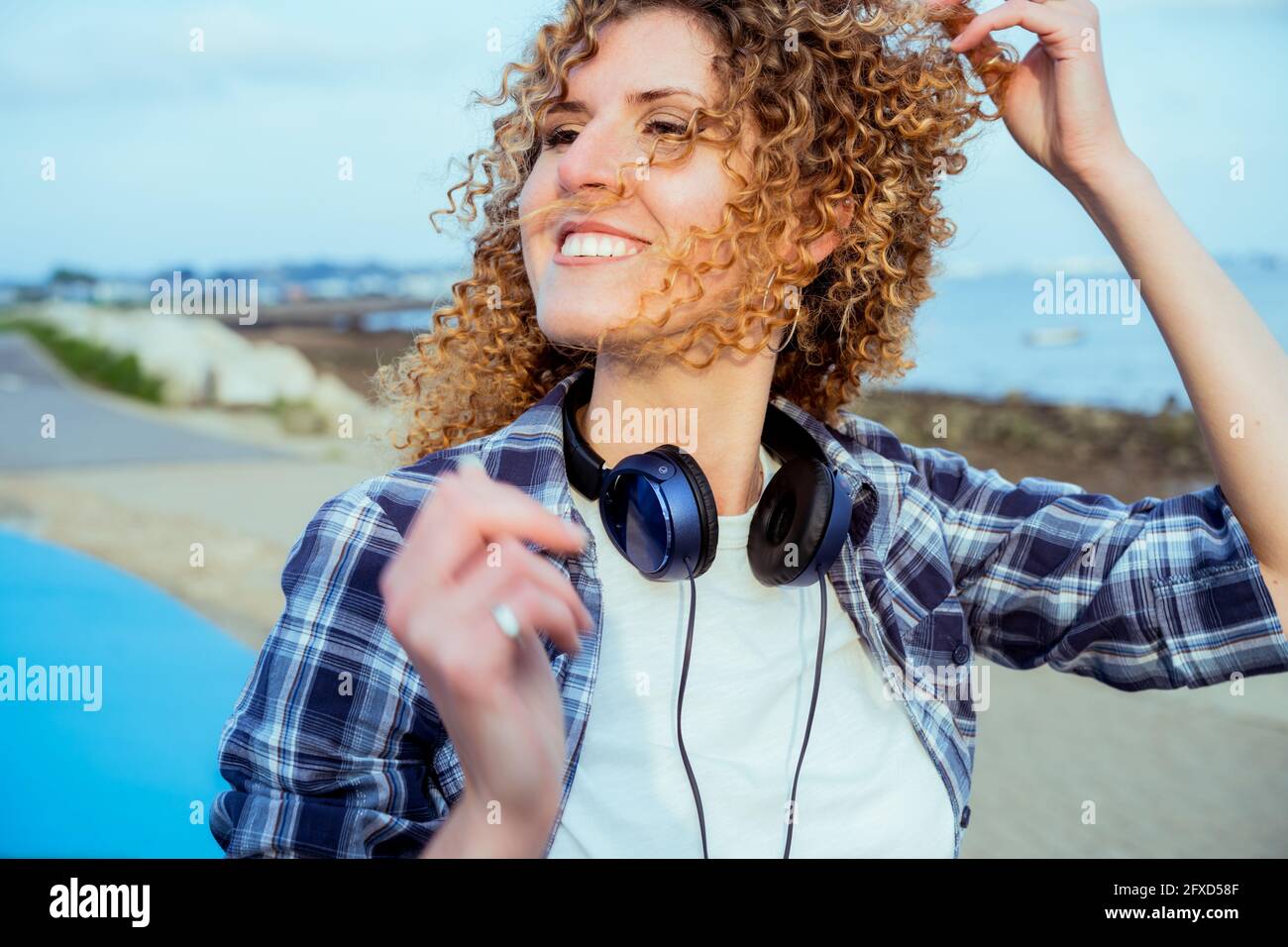 Nahaufnahme Porträt einer lächelnden, lockigen kaukasischen Frau mit großen Kopfhörern, die im Freien läuft. Genießen Sie den Moment und die Musik. Freiheit und Glück Stockfoto
