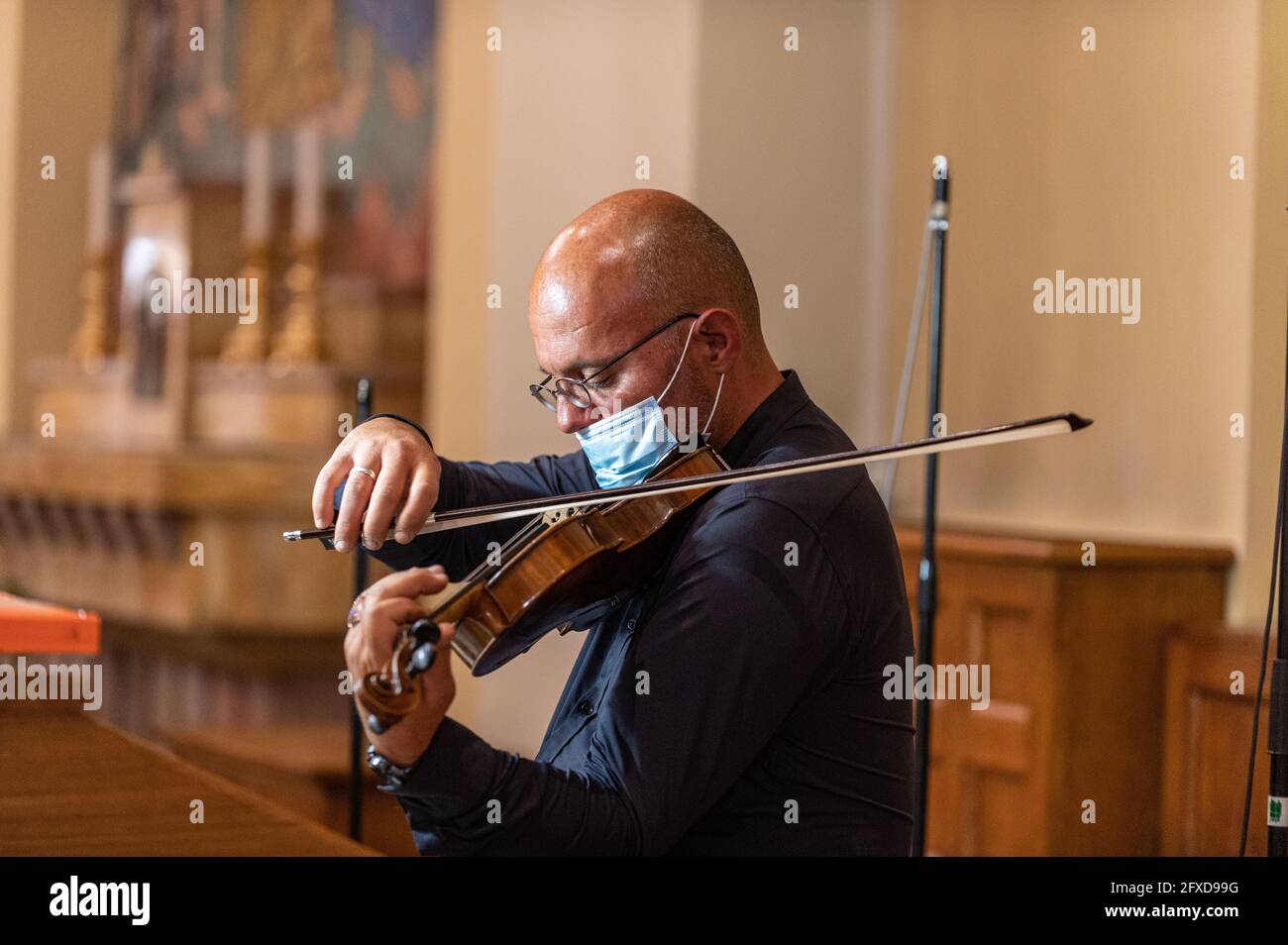 Geiger in der Kirche mit medizinischer Maske, die Geige spielt Stockfoto