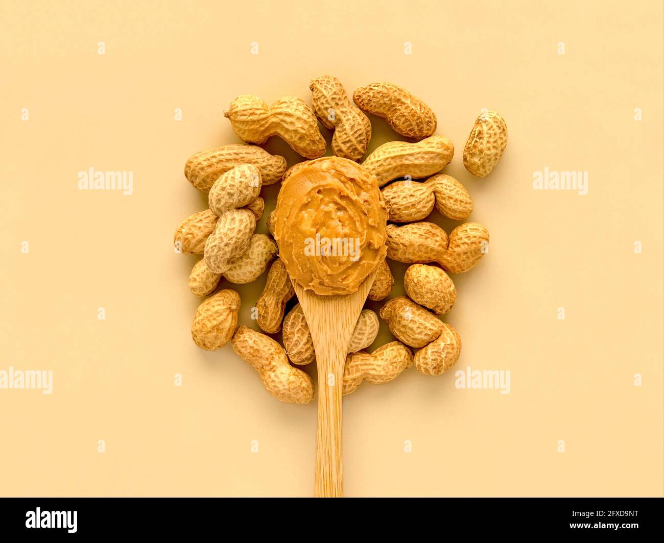 Erdnüsse und Erdnussbutter in Bambuslöffel aus Holz auf beige Hintergrund Stockfoto