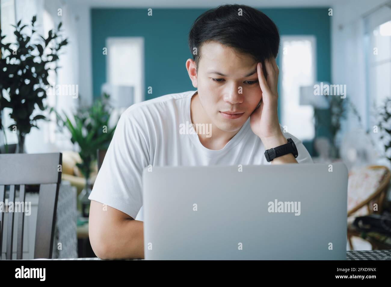 Nachdenklicher, ernsthafter junger Mann, der Online-Probleme löst und dabei resear Stockfoto