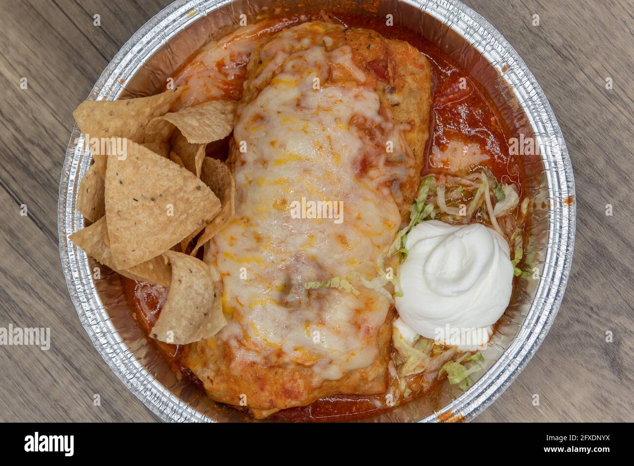 Blick von oben auf den feuchten Burrito, der in geschmolzenem Käse erstickt und mit Reis und saurer Rahm in einer großen Dose serviert wurde. Stockfoto