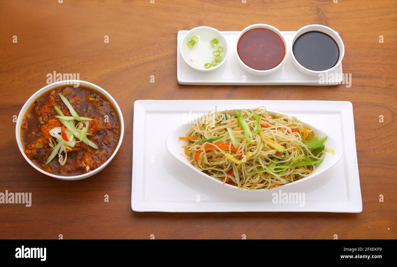 Chicken Hakka Noodles in einer ovalen, weißen Schale angeordnet Auf einem weißen Servierbrett mit Huhn Chili Masala und Verschiedene Saucen als Kombination wi Stockfoto